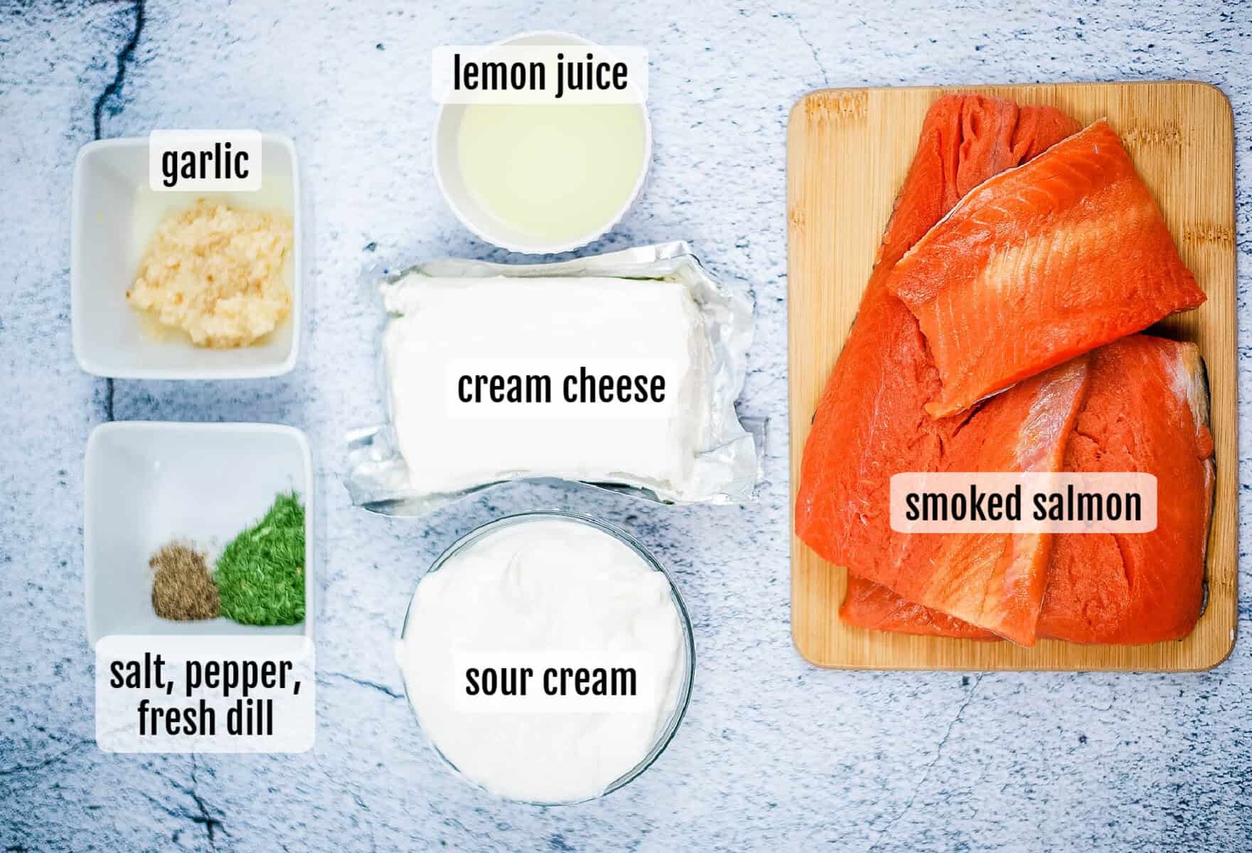Top view of smoked salmon dip ingredients, including smoked salmon, cream cheese, sour cream, lemon juice, minced garlic, plus salt, pepper, and fresh dill, all arranged on a light surface.