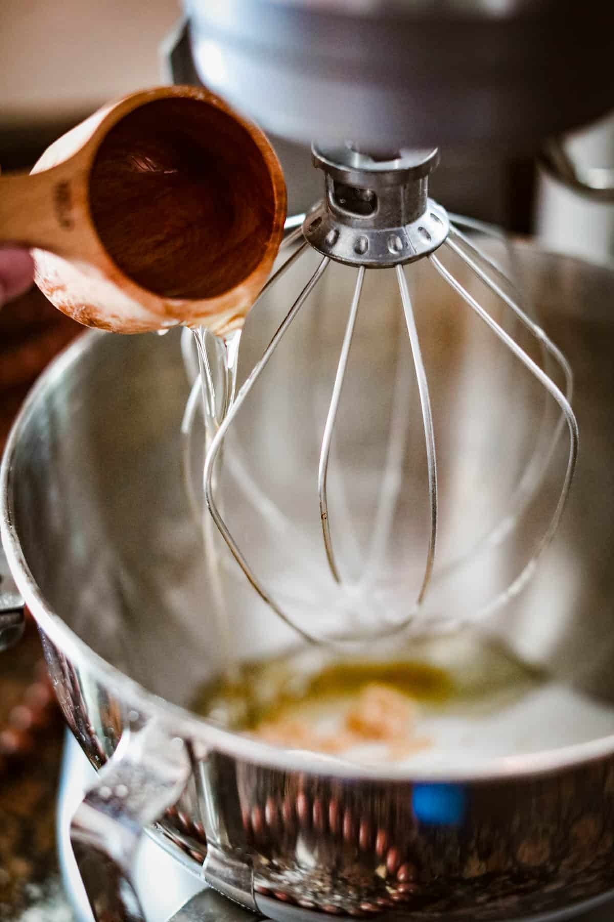 A person mixing apple cider and donut ingredients in a bowl with a wooden spoon.