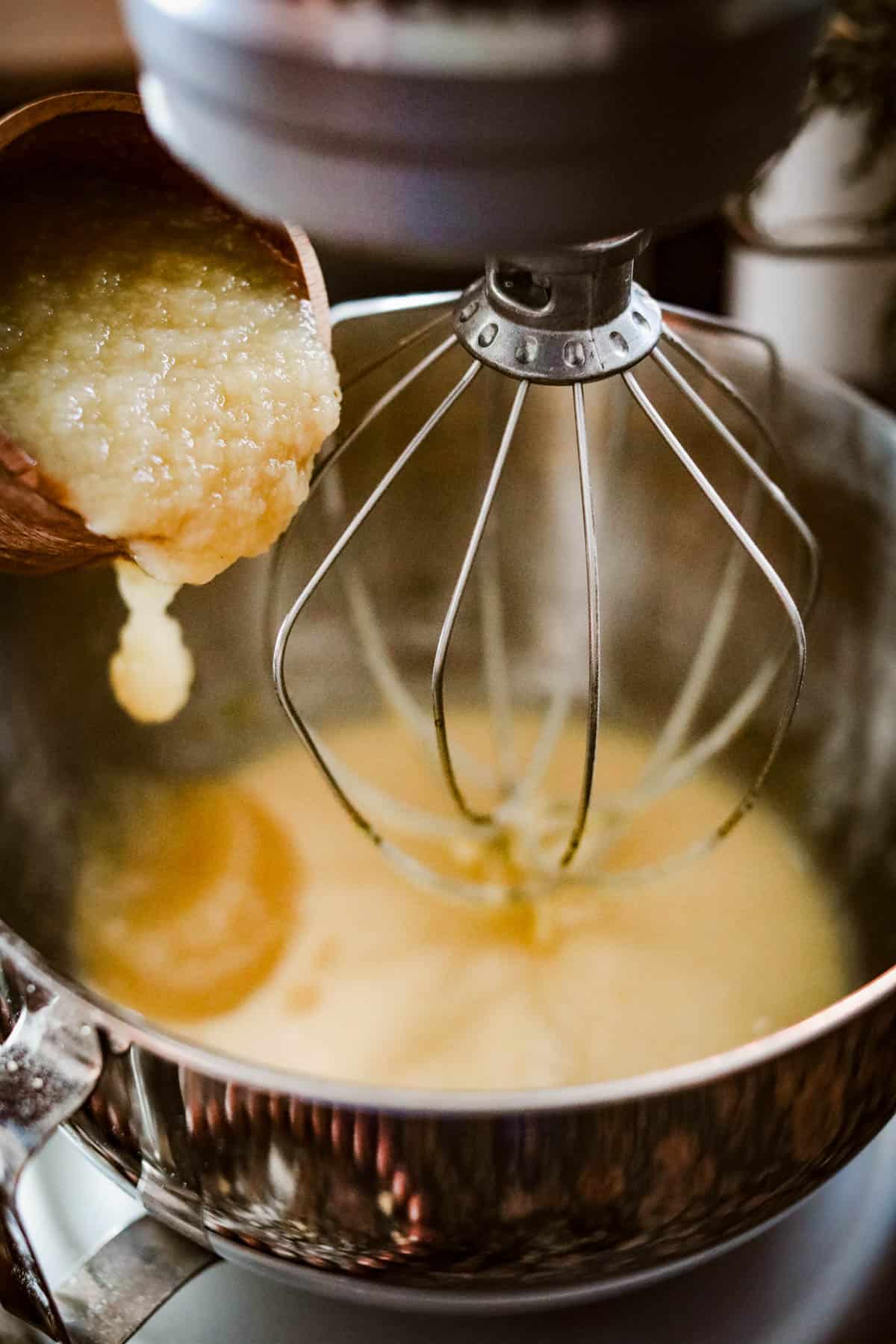A bowl of batter for an apple cider donut cake being mixed with a wooden spoon.