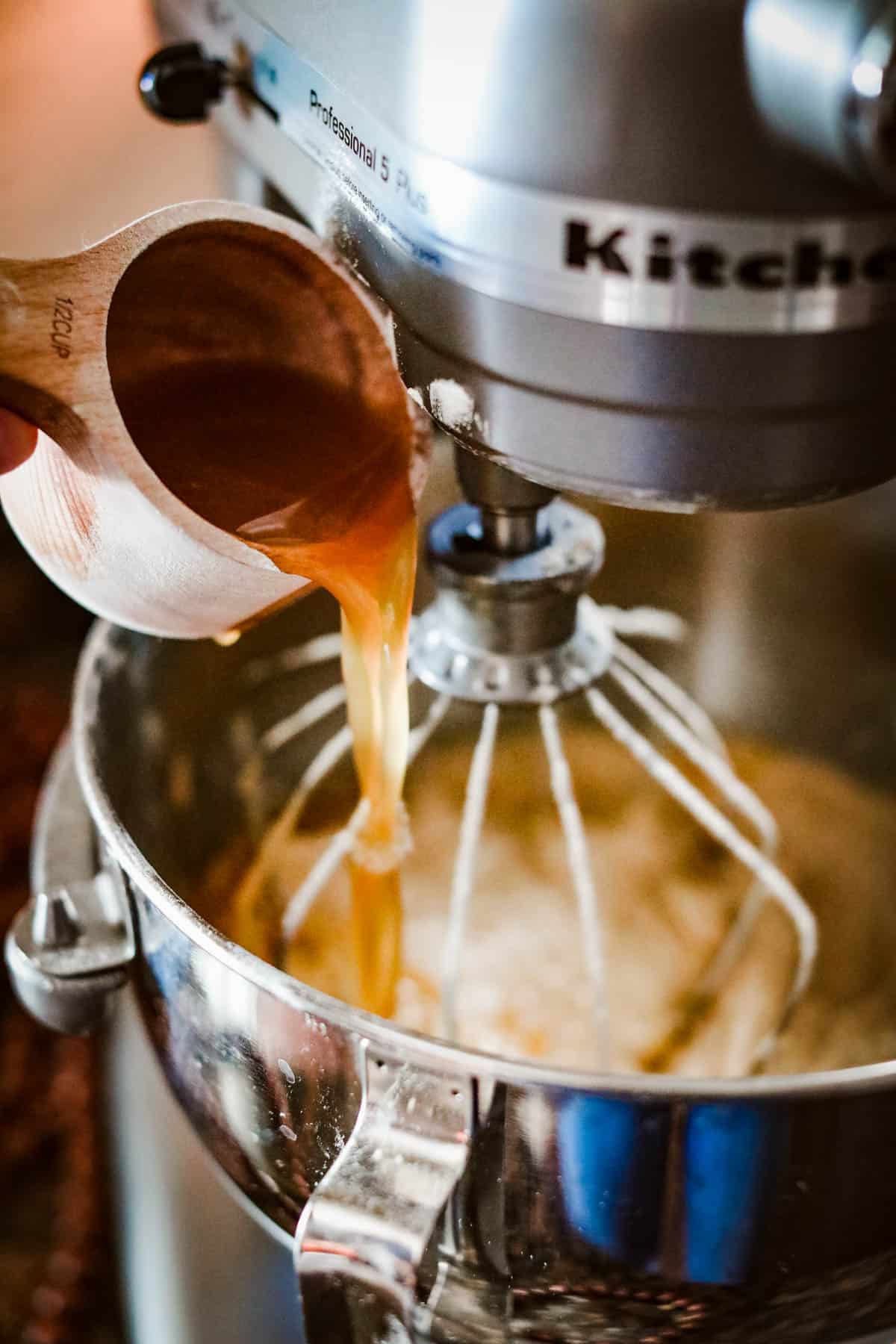 A person pouring caramel over an apple cider donut cake in a kitchen mixer.