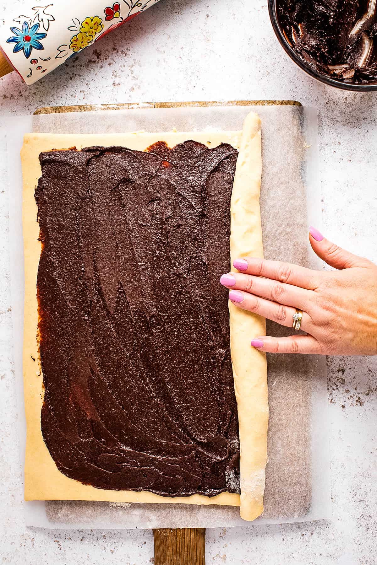 A person spreading chocolate frosting on a chocolate babka.