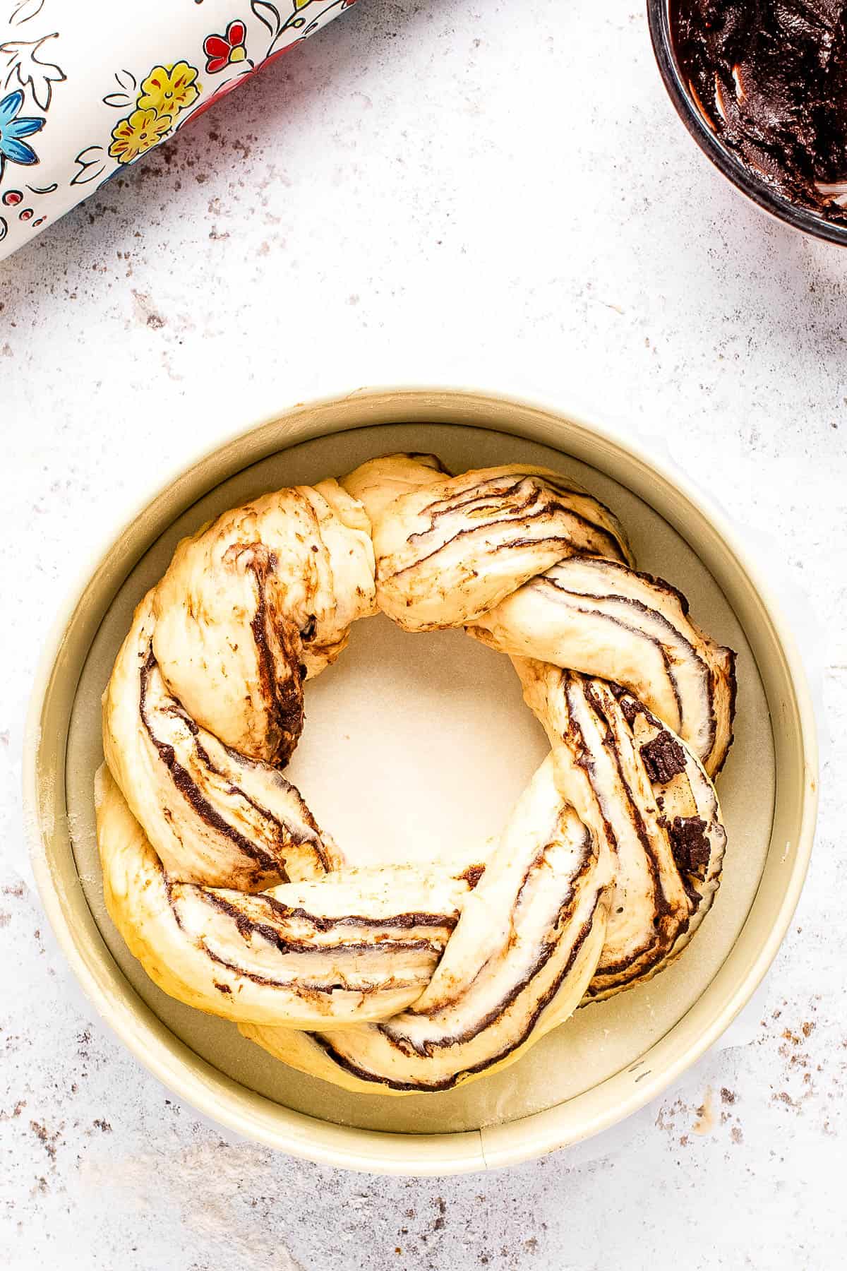 A braided chocolate babka in a white bowl next to a roll of wrapping paper.