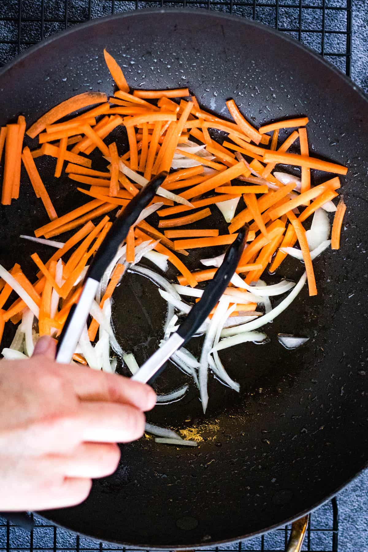 A person preparing beef yakisoba by slicing carrots in a wok.