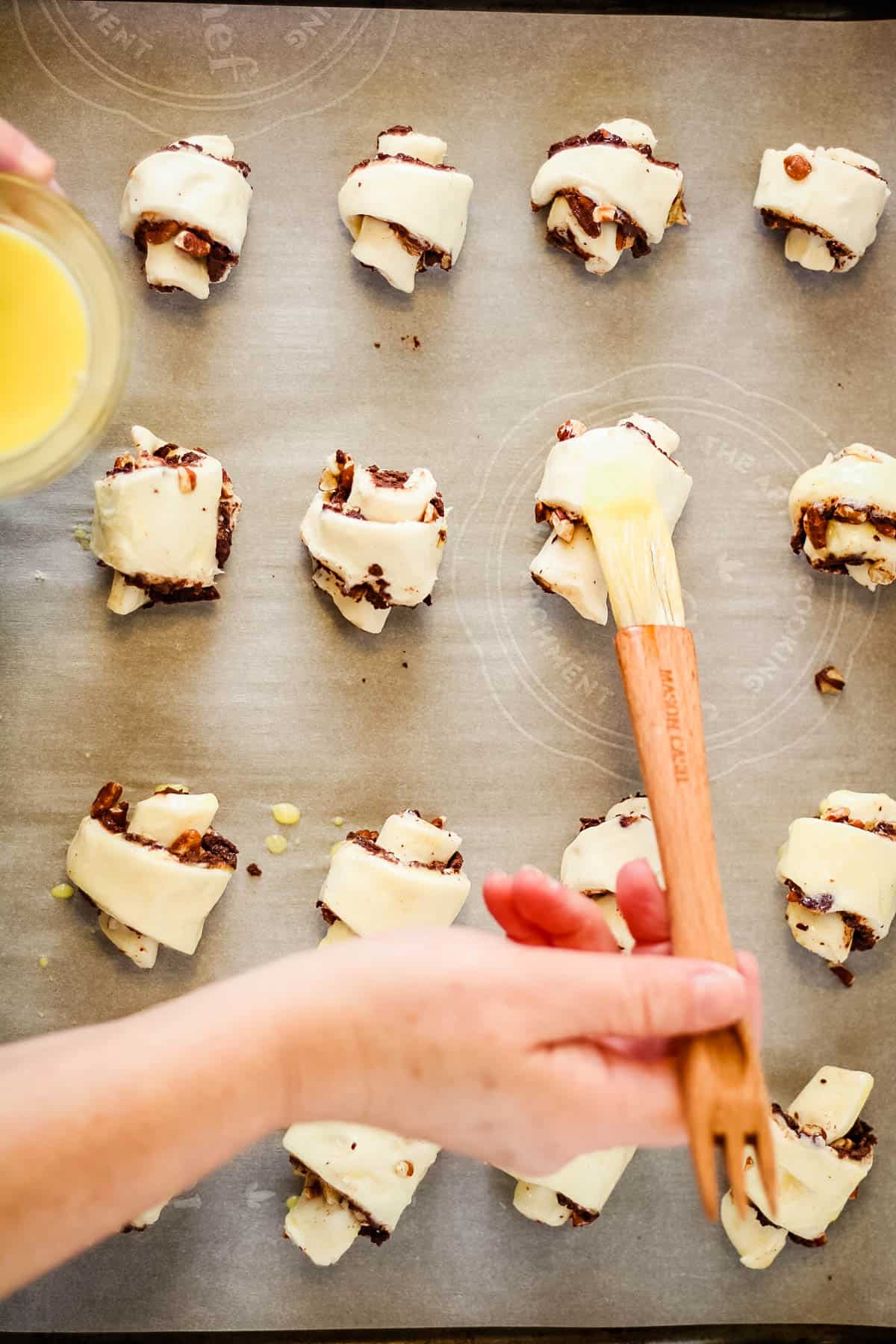A person is dipping a wooden spoon into rugelach dough on a baking sheet.