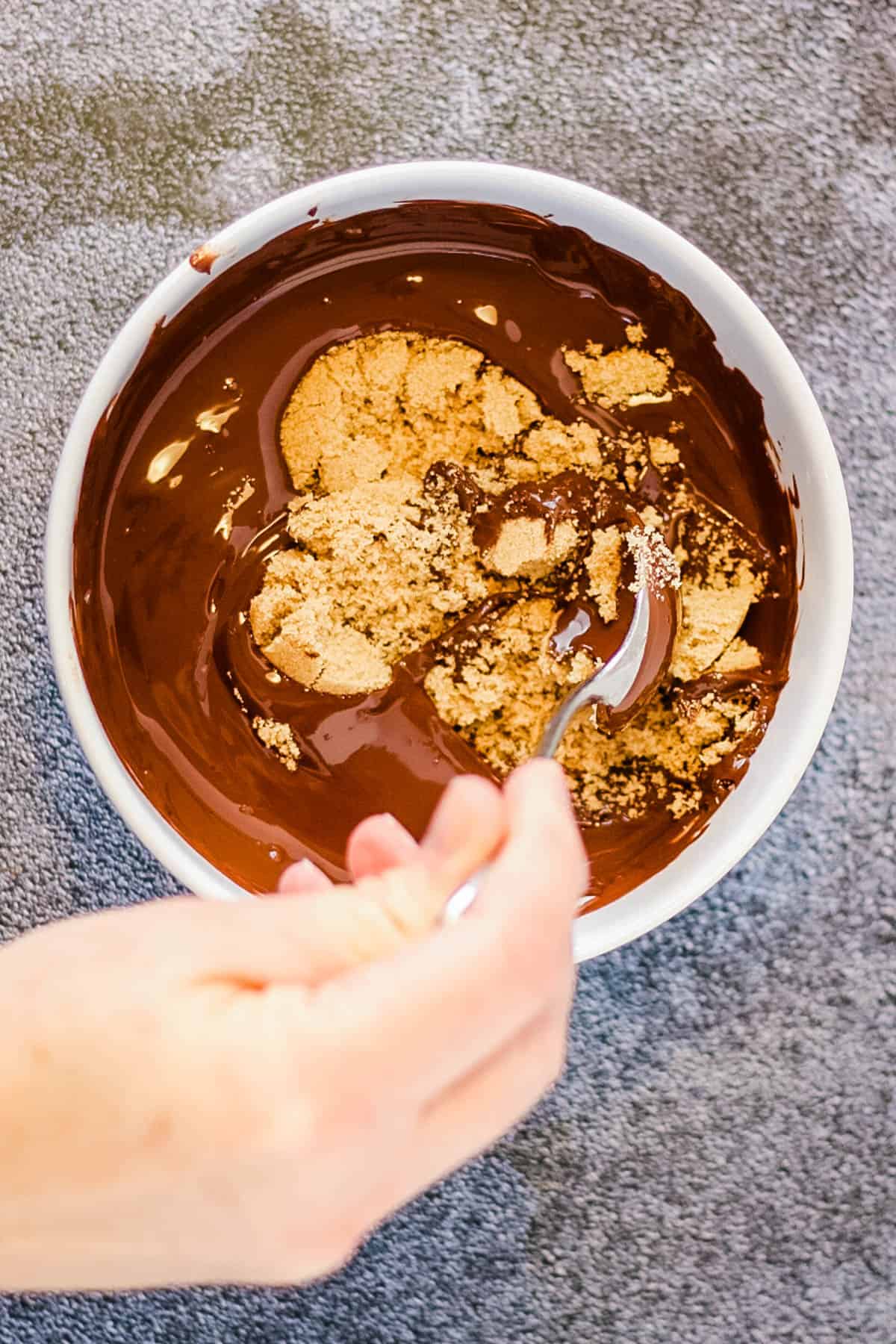 A person holding a spoon in a bowl of chocolate and enjoying rugelach.