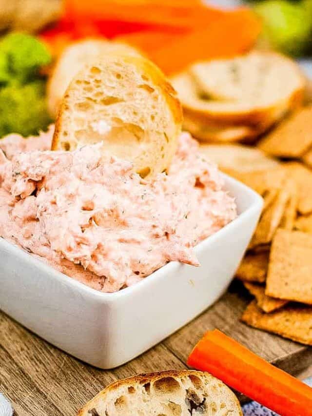 A bowl of tuna dip with crackers and carrots.