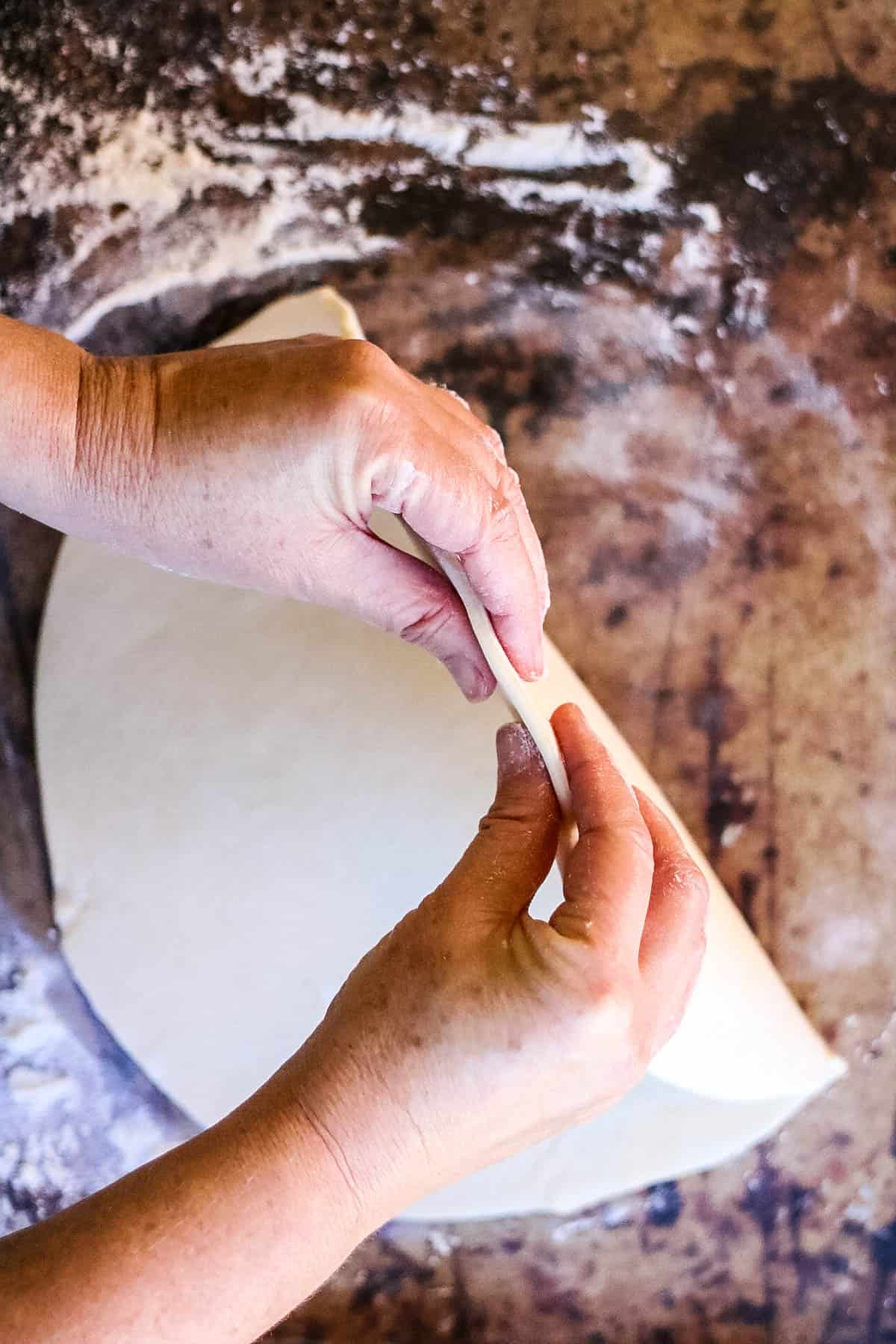 A person preparing rugelach dough on a table.