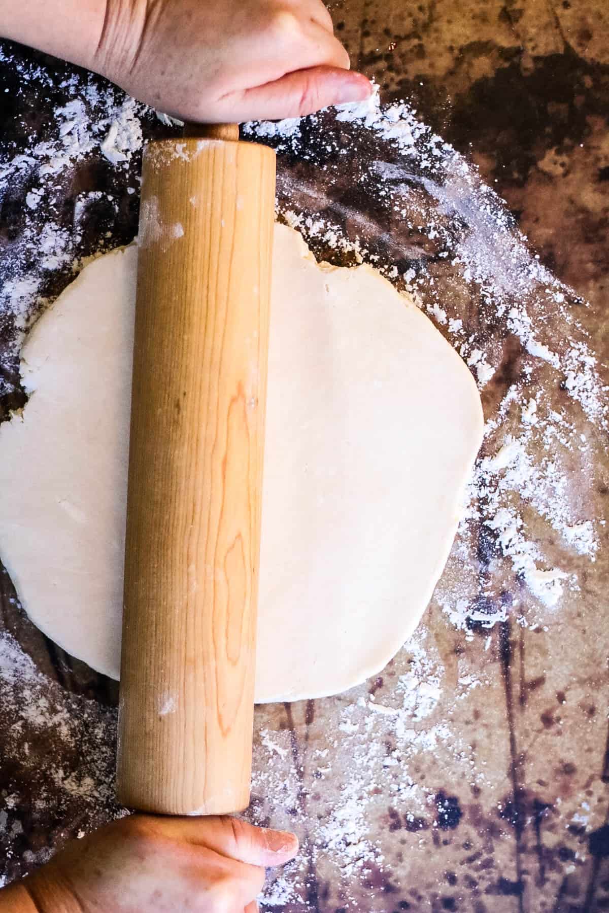 A person preparing rugelach dough on a floured surface.