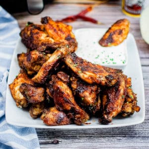 low angle shot of a pile of bbq chicken wings on a white platter with ranch dressing for dipping