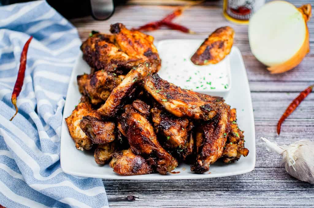 low angle shot of a pile of bbq chicken wings on a white platter with ranch dressing for dipping