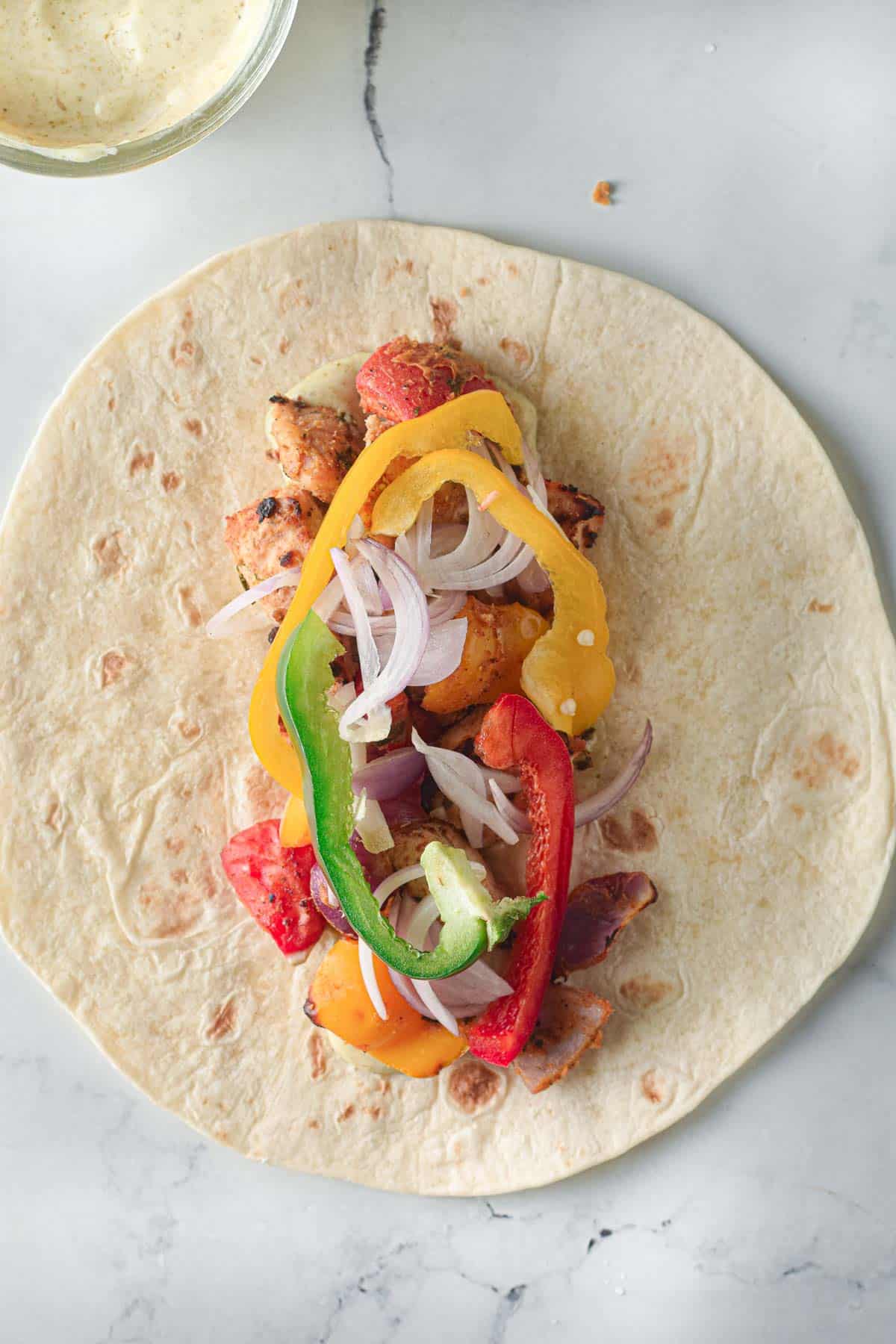 A chicken tikka wrap with peppers and onions.