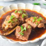 Close up low angle shot of cooked chicken adobo on serving plate.