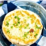 A close-up of a cheese arepa, inspired by a traditional arepas recipe, topped with chopped herbs on a blue and white cloth, presented on a metal plate.