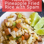 A plate of pineapple fried rice features diced Spam, juicy pineapple chunks, green onions, and lime wedges on the side.