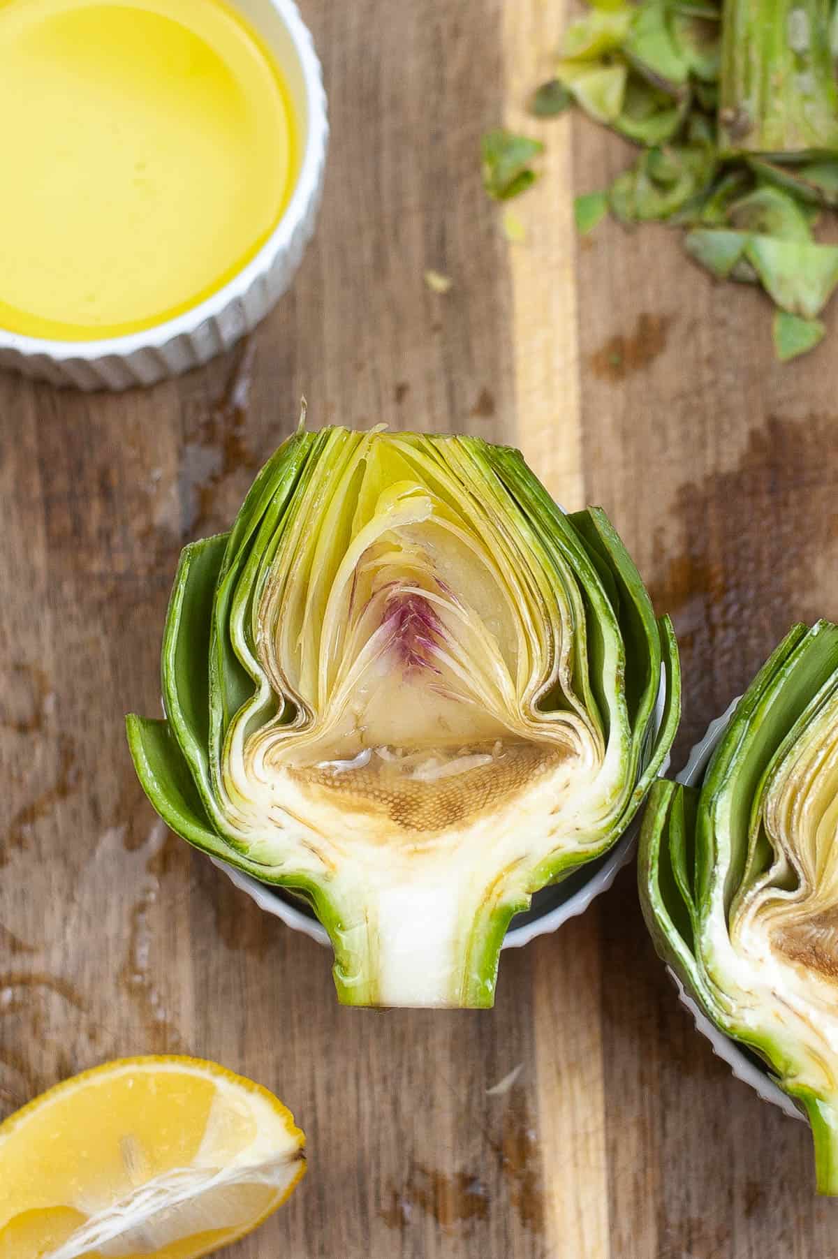 Air-fried artichokes served with lemon wedges on a wooden cutting board.