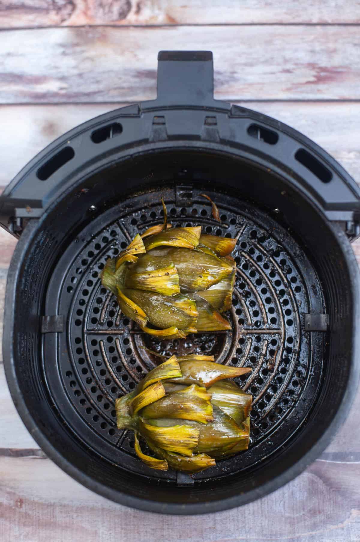 Artichokes cooked in an air fryer on a wooden table.