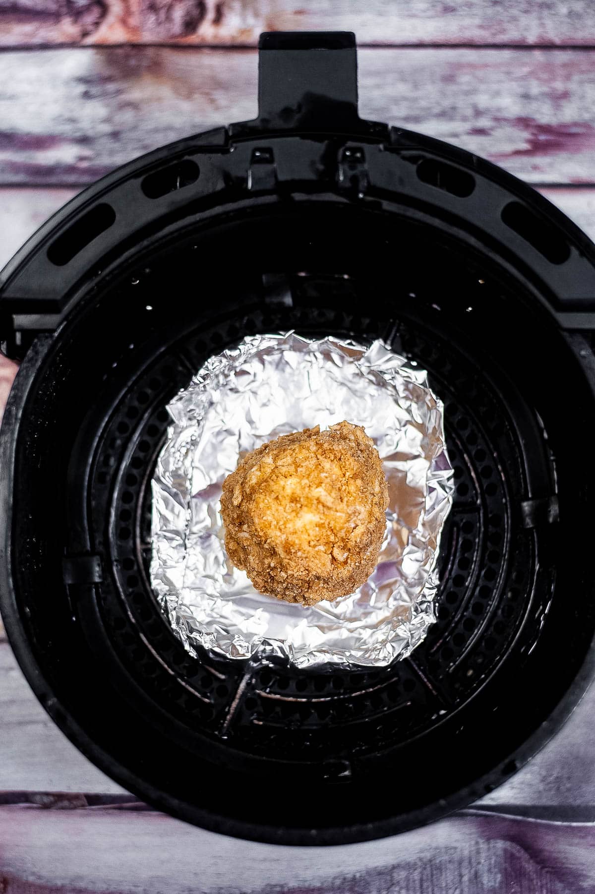 coated ice cream ball on foil in the air fryer basket.