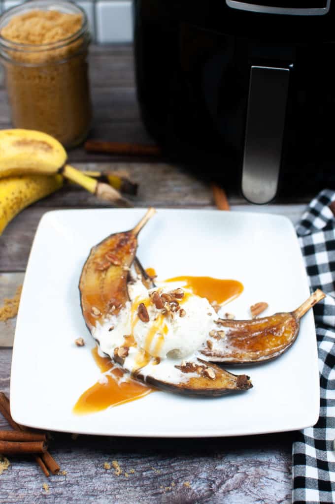 low angle shot of air fryer bananas on a white plate with vanilla ice cream and caramel drizzle.