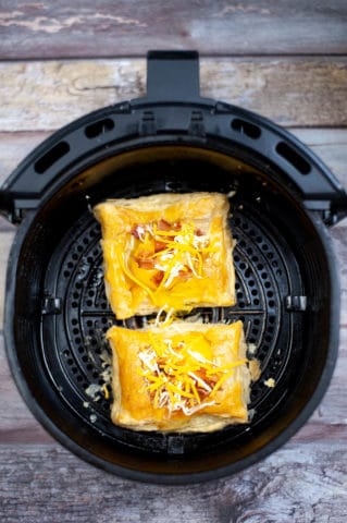 Two breakfast pizzas sizzling in an air fryer on a wooden table.