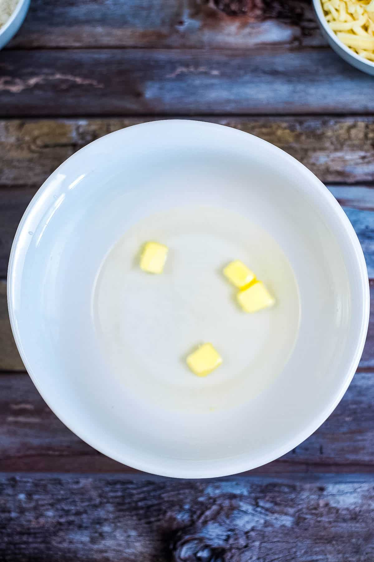 A white bowl filled with butter and cheese, part of an arepas recipe, on a wooden table.
