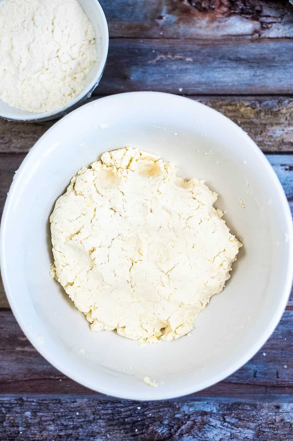 A bowl of dough and a bowl of flour on a wooden table for an arepas recipe.
