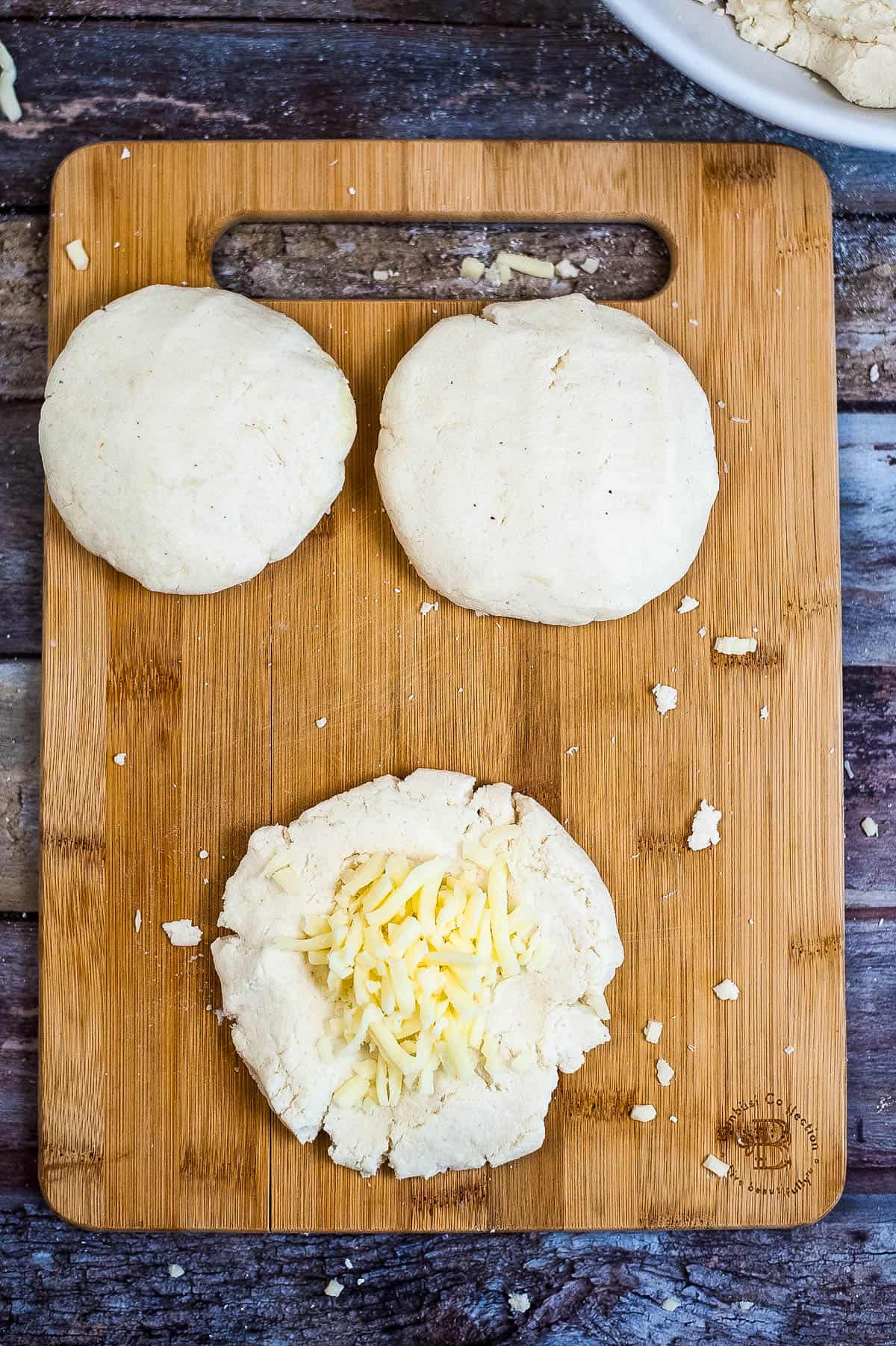A wooden cutting board with dough and cheese for an arepas recipe.