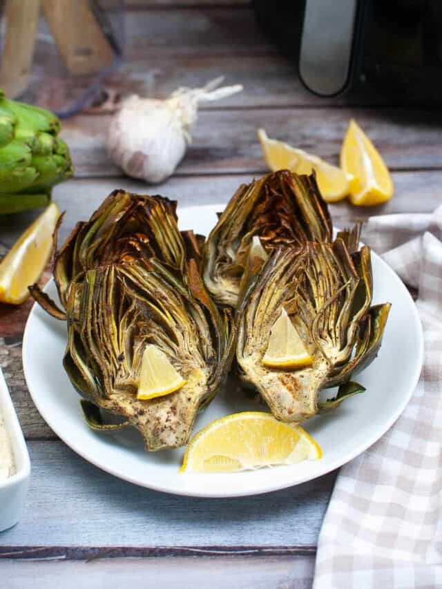 Roasted artichokes on a plate with lemon wedges.