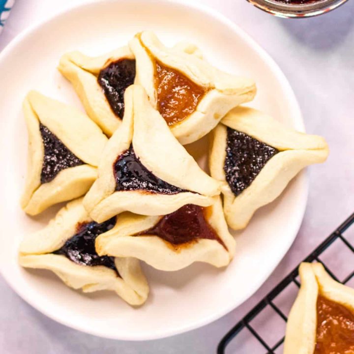 Overhead shot of a pile of hamentashen cookies on a plate.