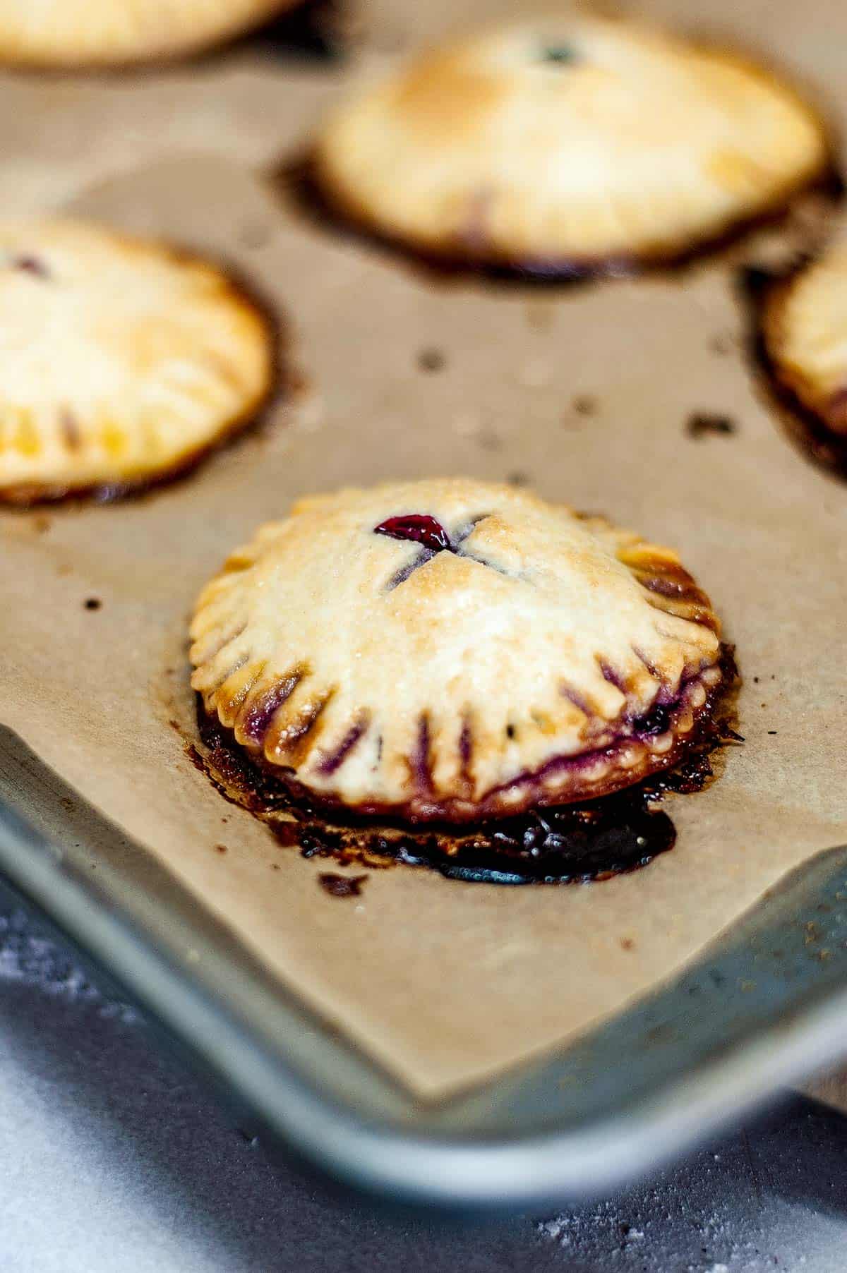 low angle closeup shot of mixed berry hand pies on a parchment lined baking sheet.