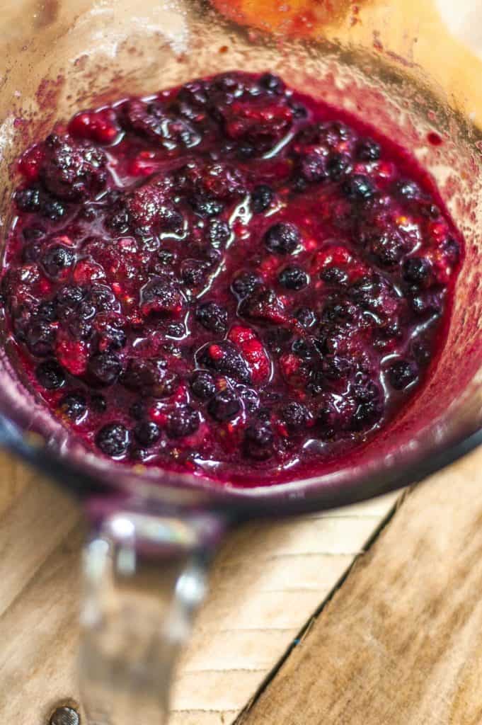 A bowl of berry sauce on a wooden table, featuring blueberries.