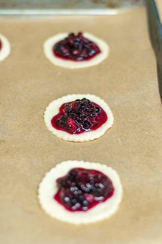 A tray of hand pies on a baking sheet, filled with blueberries.