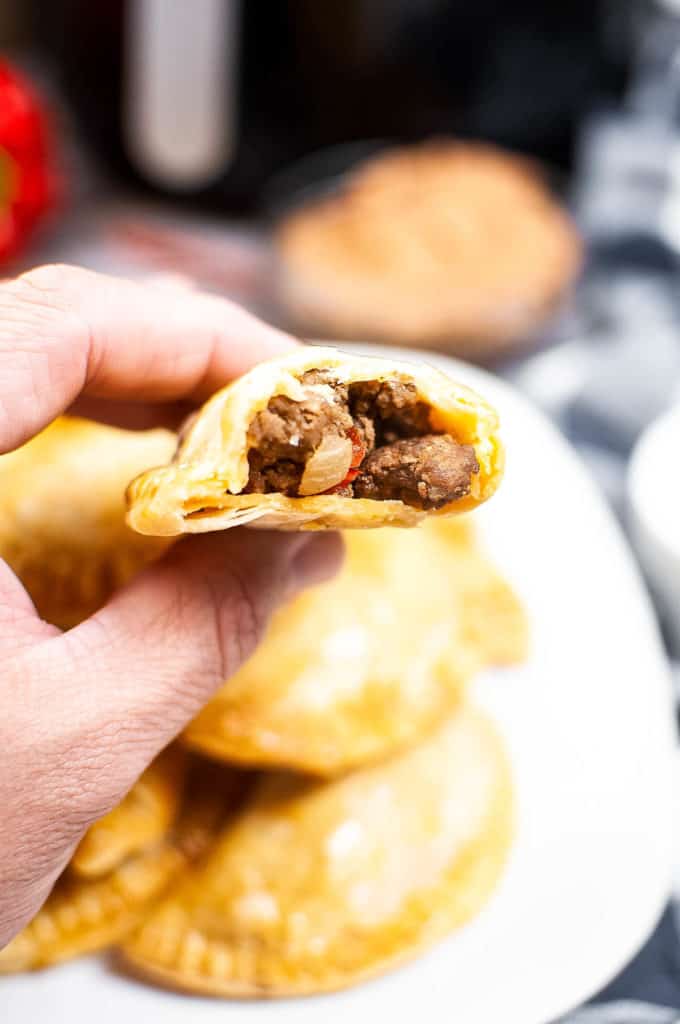 Close up of a beef-filled empanada in a person's hand. The empanada is split open so that you can see the beef filling inside.