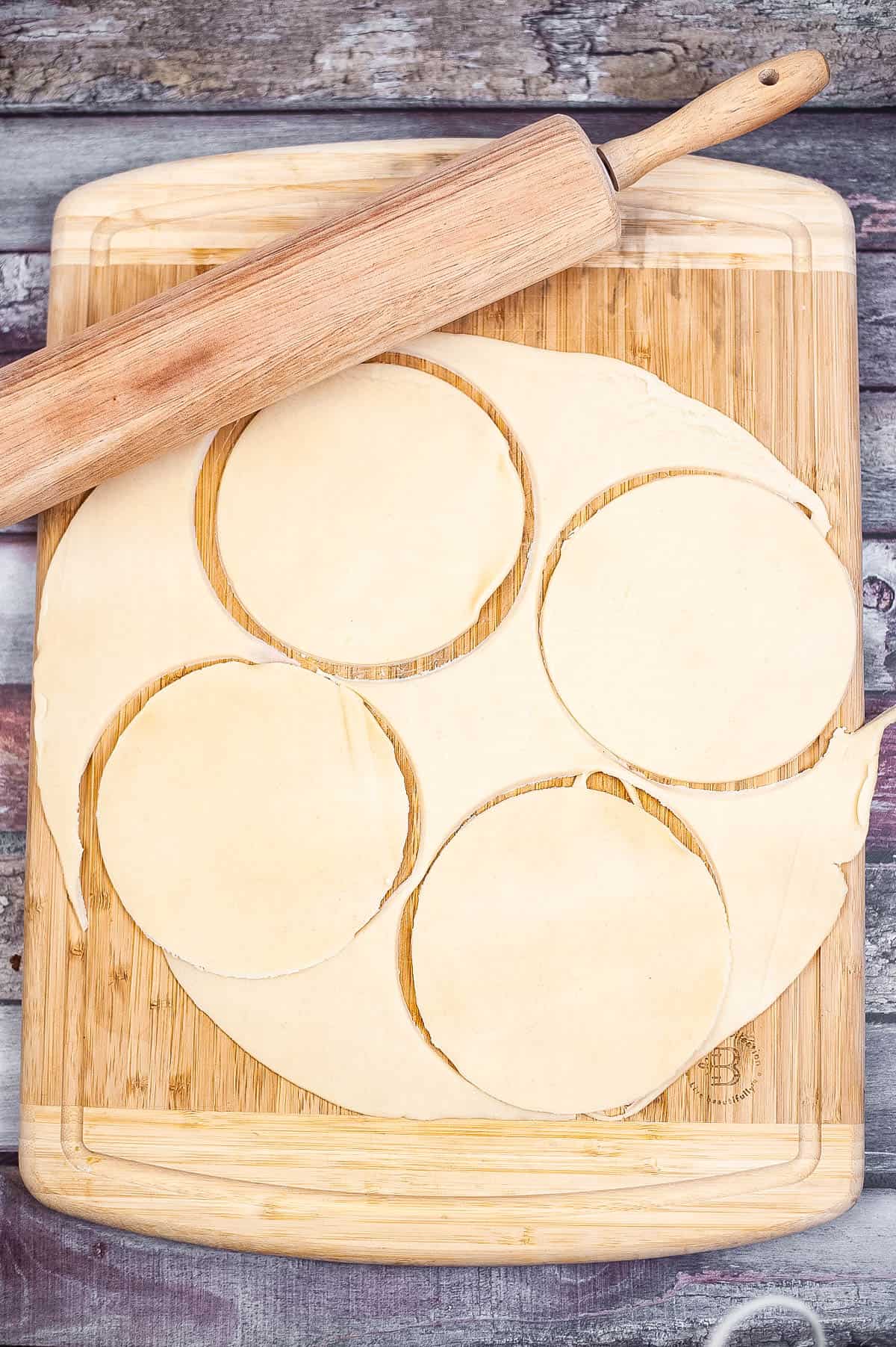 A wooden cutting board with a rolling pin, perfect for making homemade empanadas.