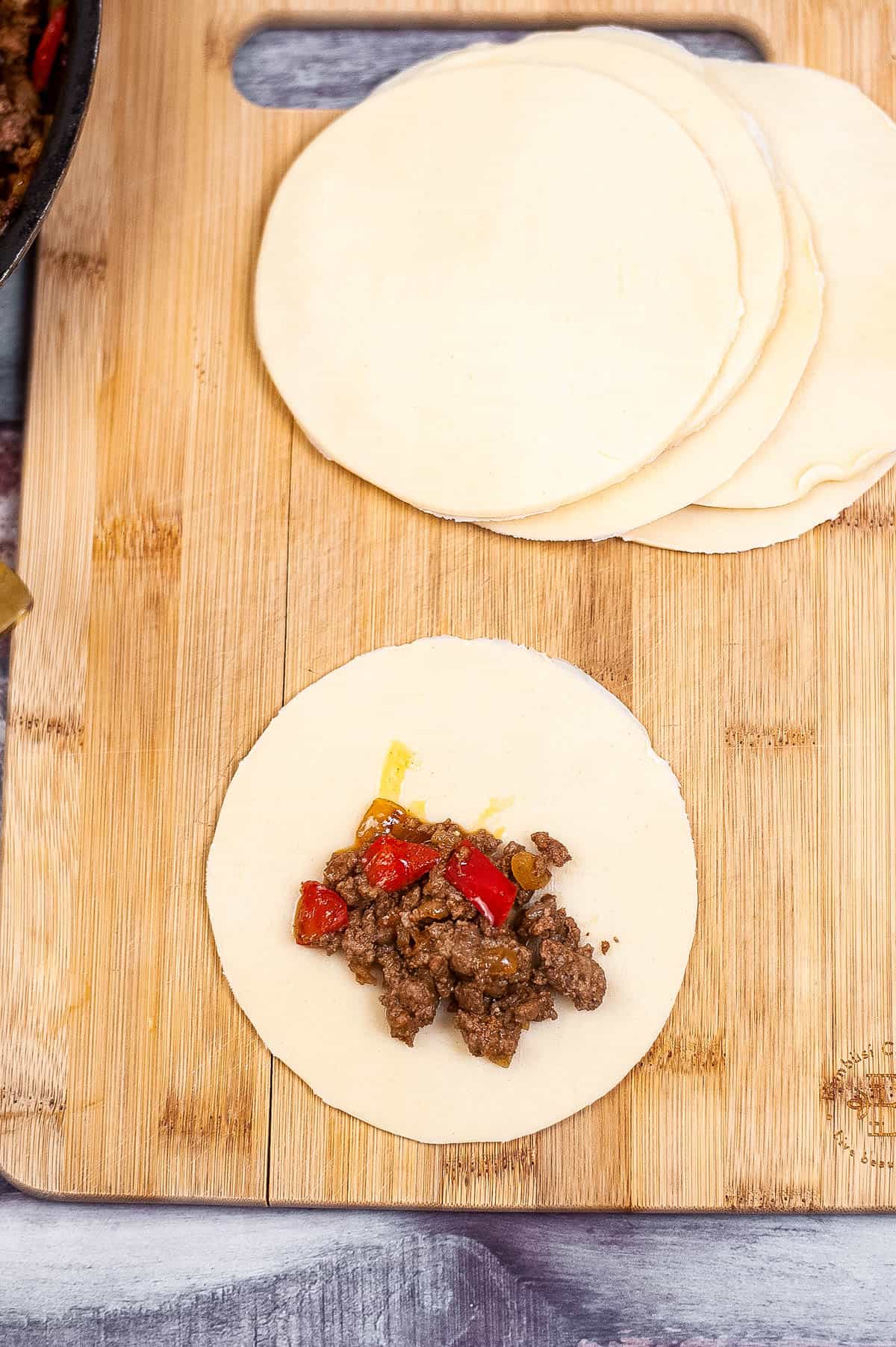 Air fryer tortillas with meat and peppers on a wooden cutting board.