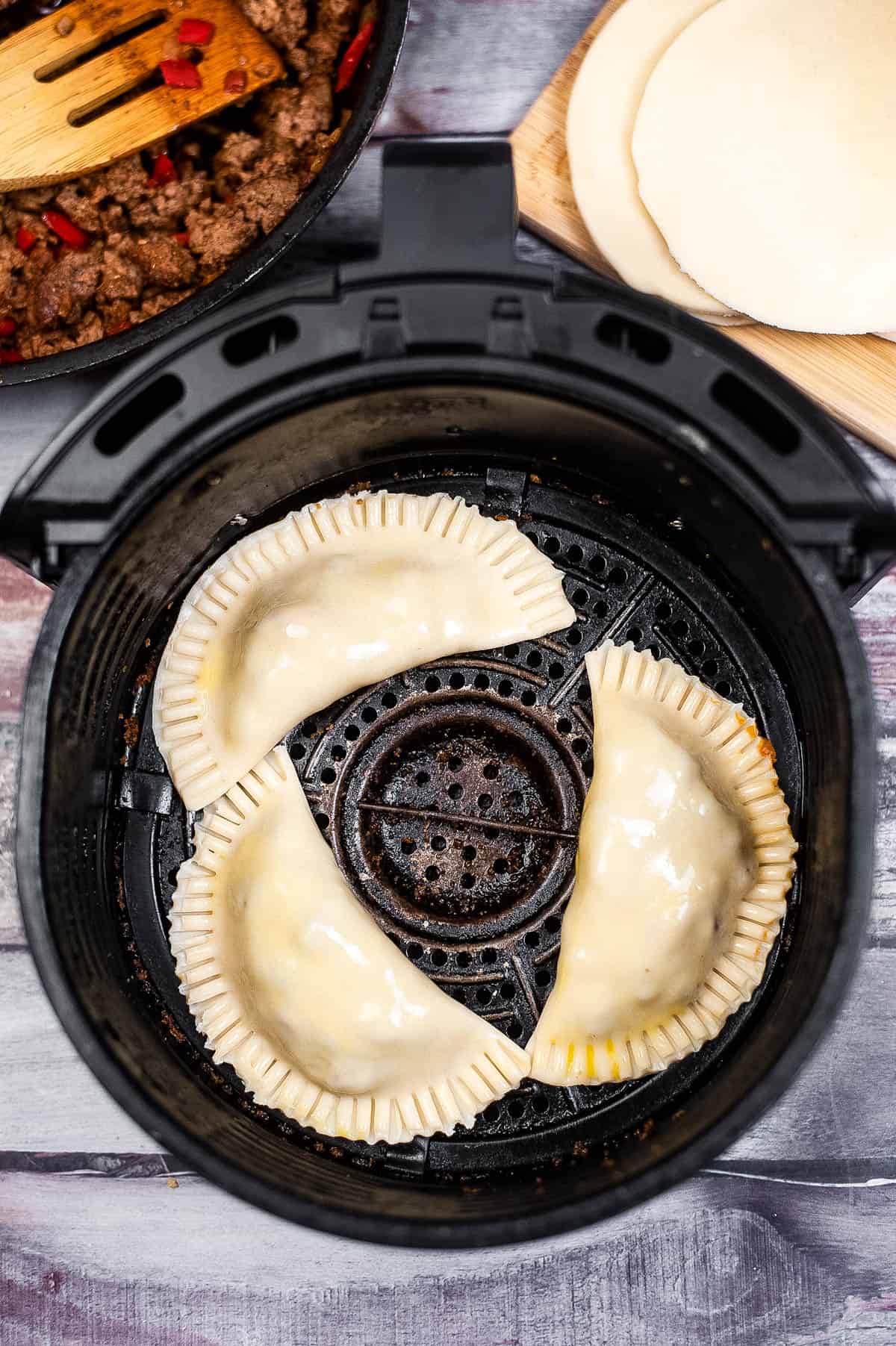 An air fryer filled with meat and empanadas.