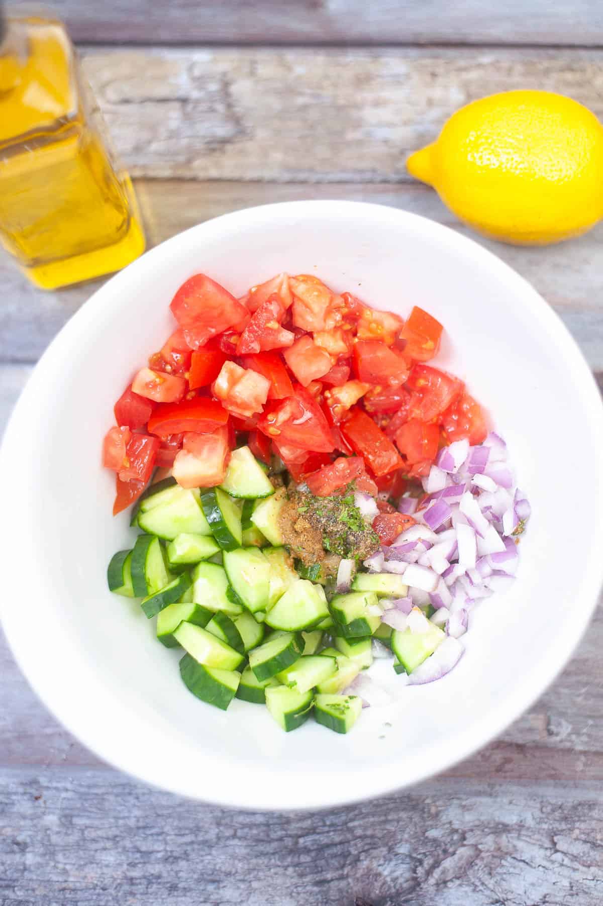 A white bowl with tomatoes, cucumbers, and lemons alongside air fryer chicken shawarma.