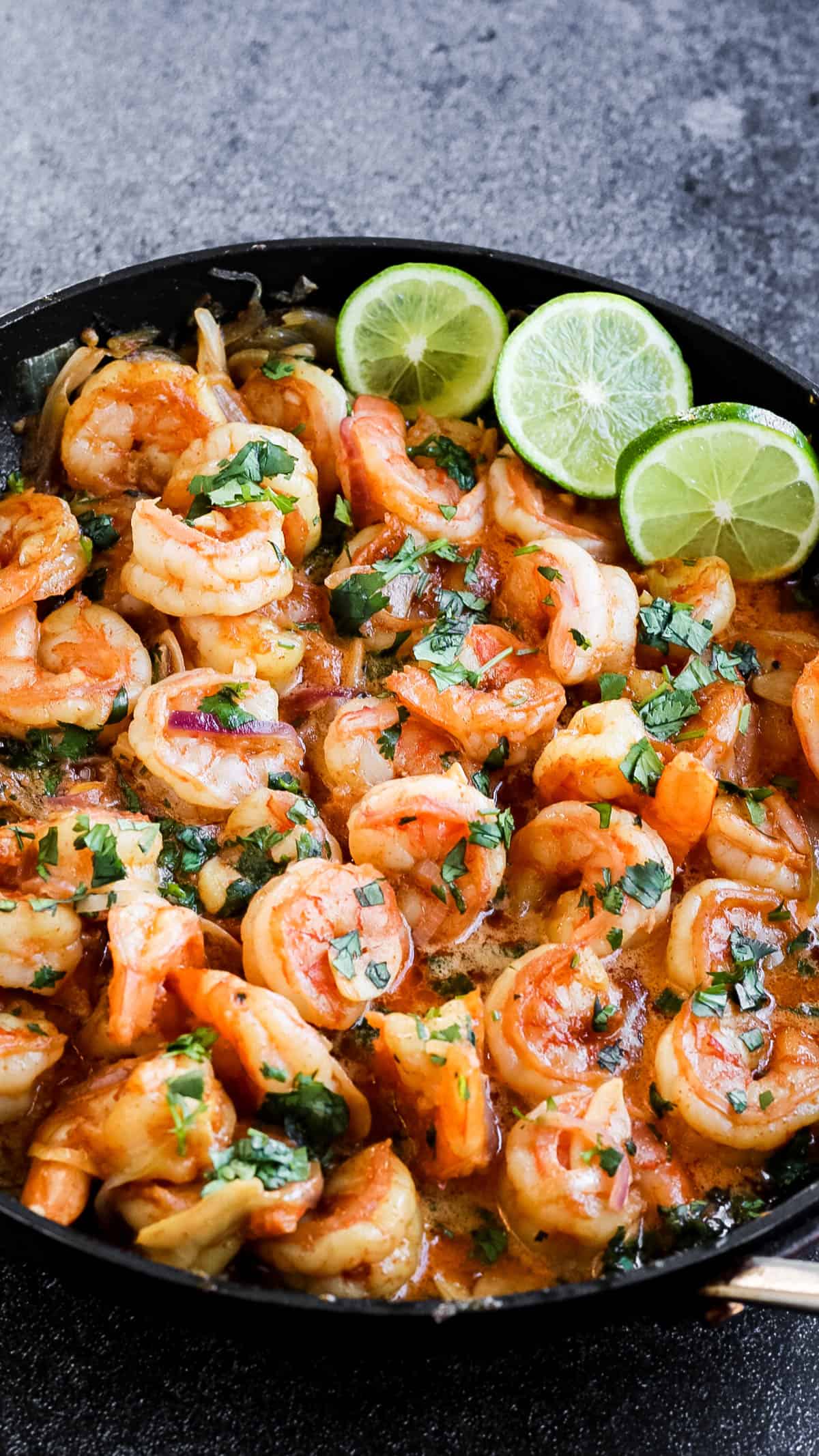 Low angle shot of mexican garlic shrimp in a skillet with lime slices.