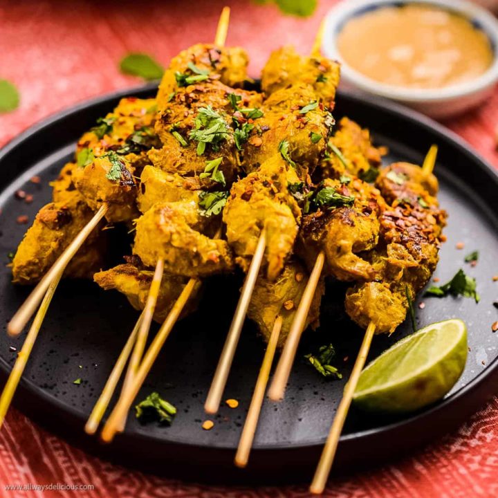 Low angle shot of thai chicken satay skewers on a black plate with peanut sauce in the background