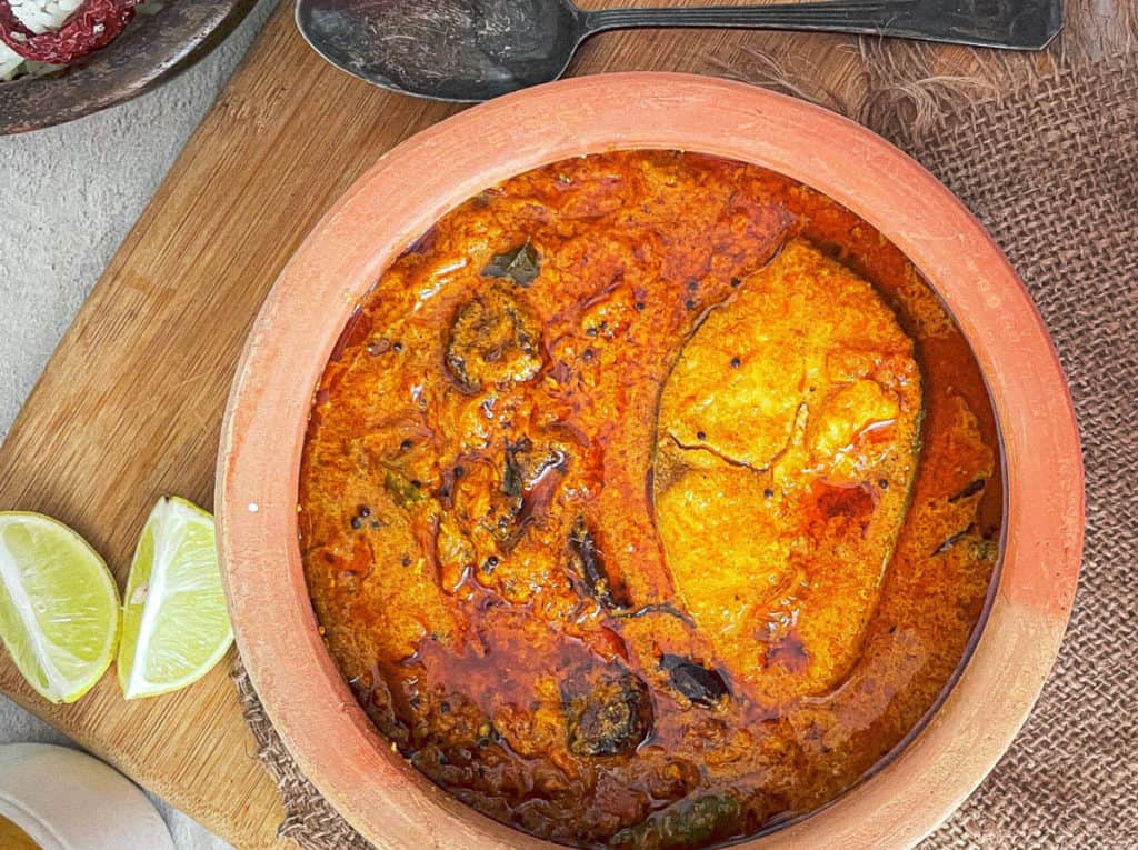 overhead shot of Kerala fish curry in an earthenware pot with lime wedges on the side.