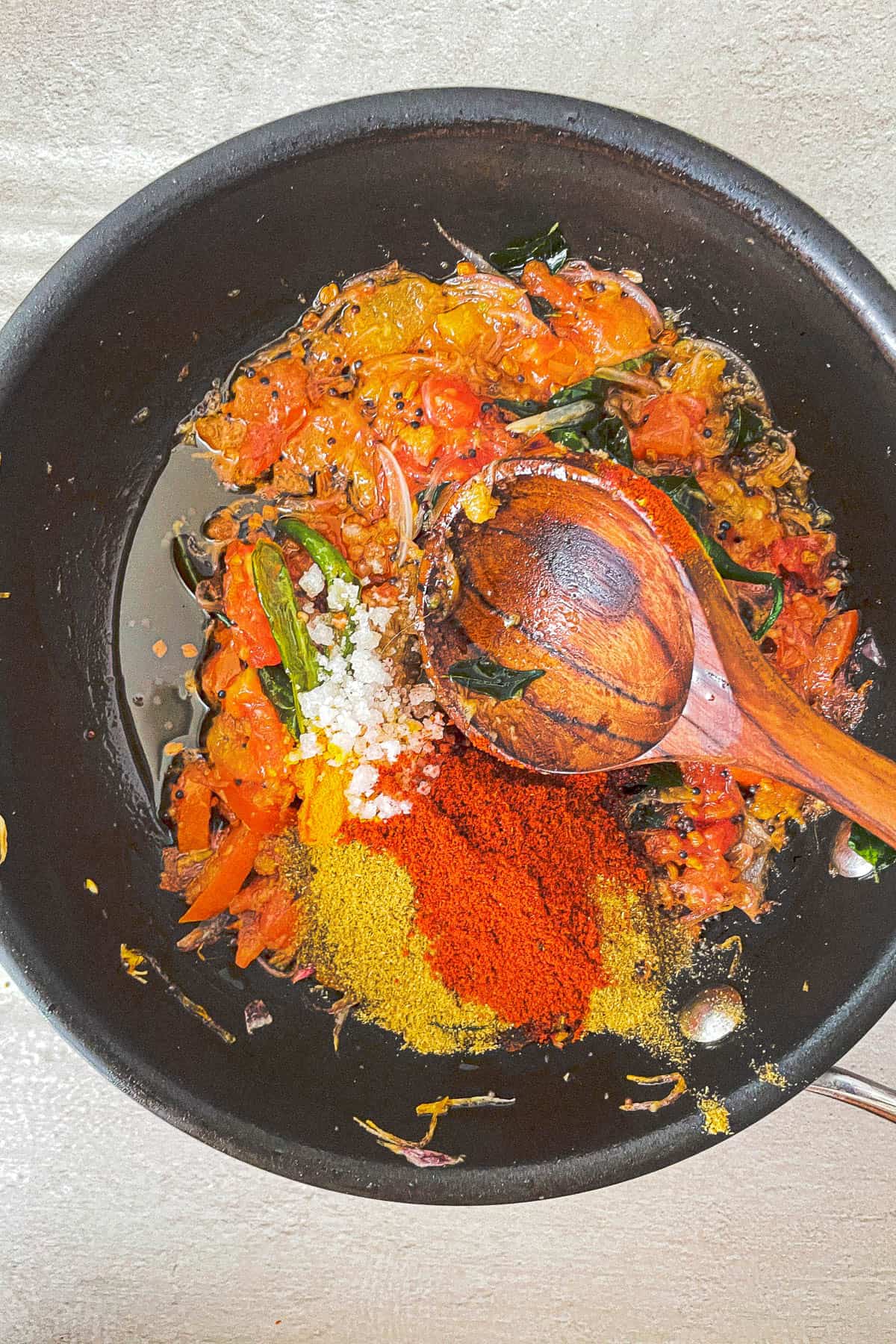 A kerala fish curry cooked in a frying pan with spices and stirred with a wooden spoon.