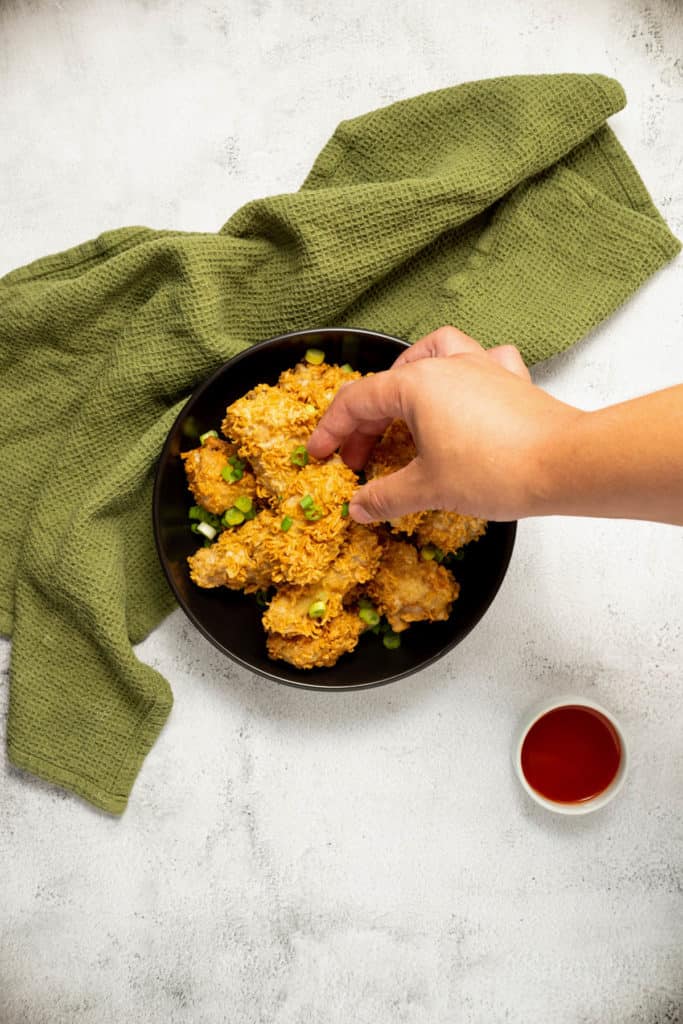 Overhead shot of a hand picking up a piece or the ramen crusted fried chicken.