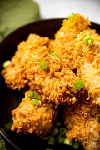 Crispy ramen fried chicken piled on a black plate and garnished with sliced green onions.