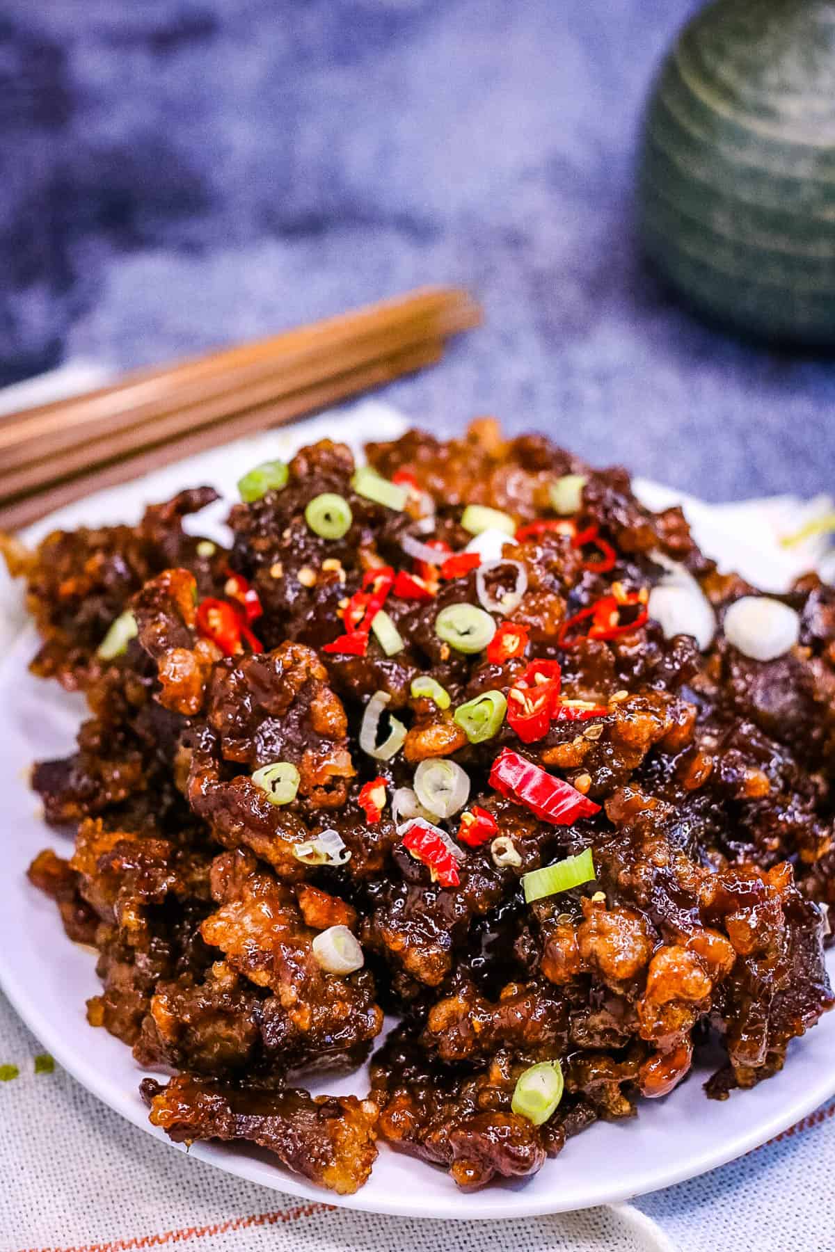Low angle shot of a plate of crispy chilli beef garnished with green onions and sliced hot red chiles.