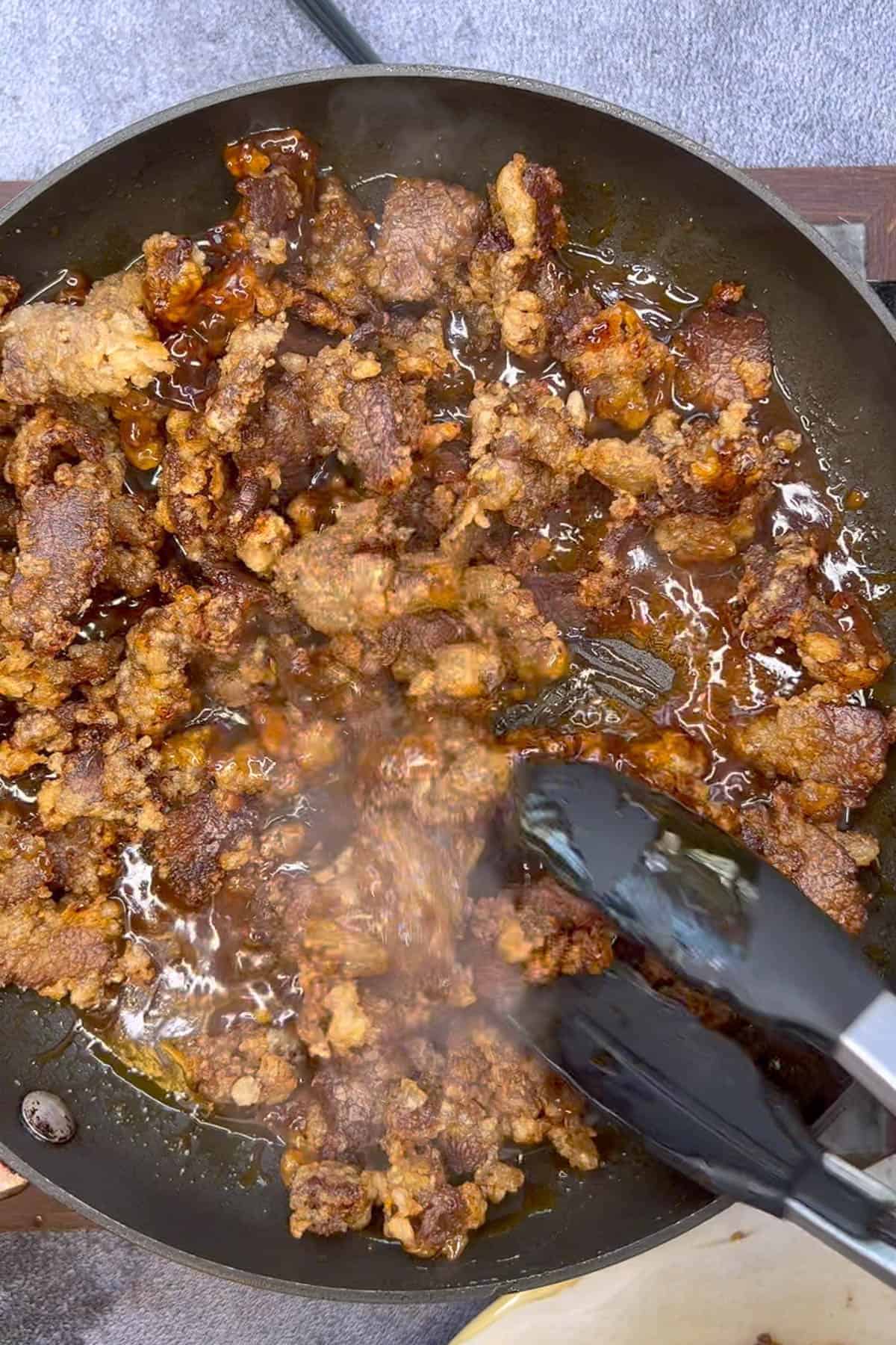 Crispy beef sizzles in a frying pan.