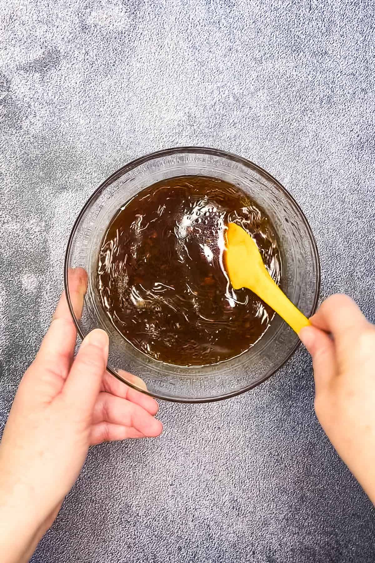 A person holding a yellow spoon over a bowl of brown sauce, serving crispy chilli beef.