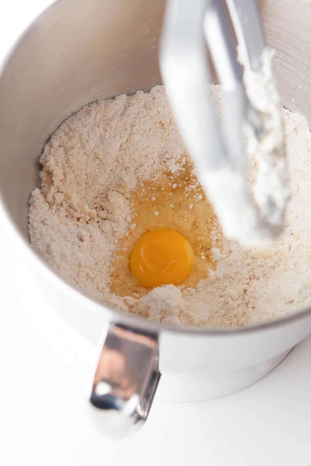 An egg is being added to flour in a mixing bowl to make dulce de leche cookies.