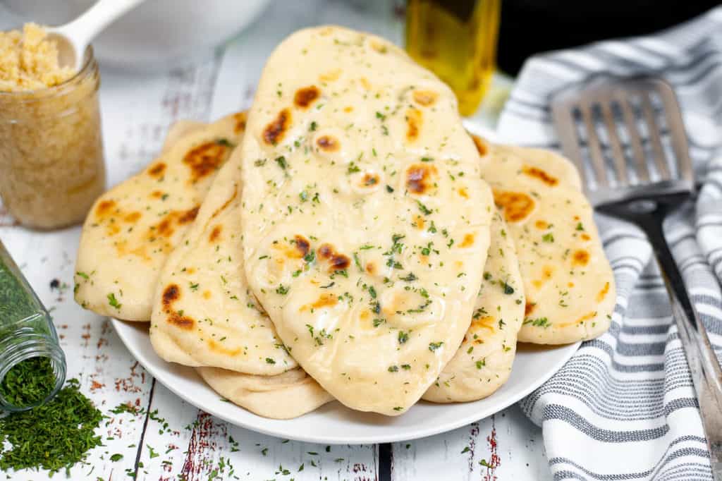 Low angle shot of butter garlic naan piled on a white plate.