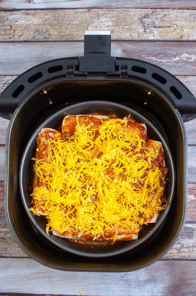 Beef and enchilada sauce on the bottom of the air-fryer pan with cheese on top.