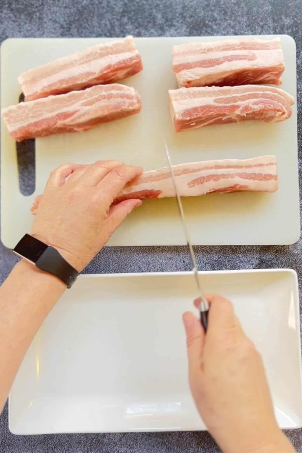 A person using an air fryer to cook pork belly slices.