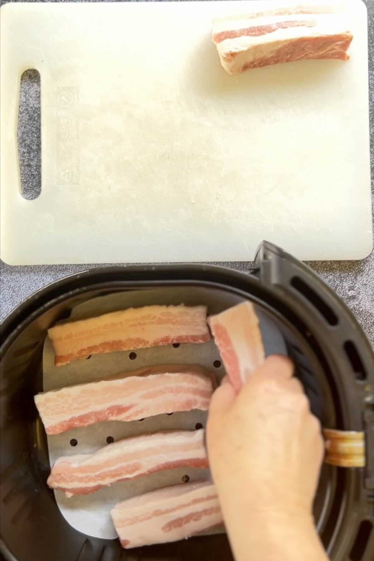 A person using an air fryer to cook pork belly.
